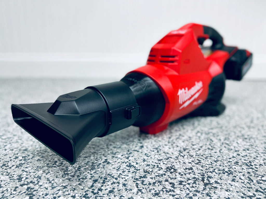 A red Milwaukee M18 FUEL Dual Battery Leaf Blower (2824-20) with a wide black nozzle is on a gray speckled floor, highlighting its compatibility with the STUBBY® Nozzle Adapter designed for this model.
