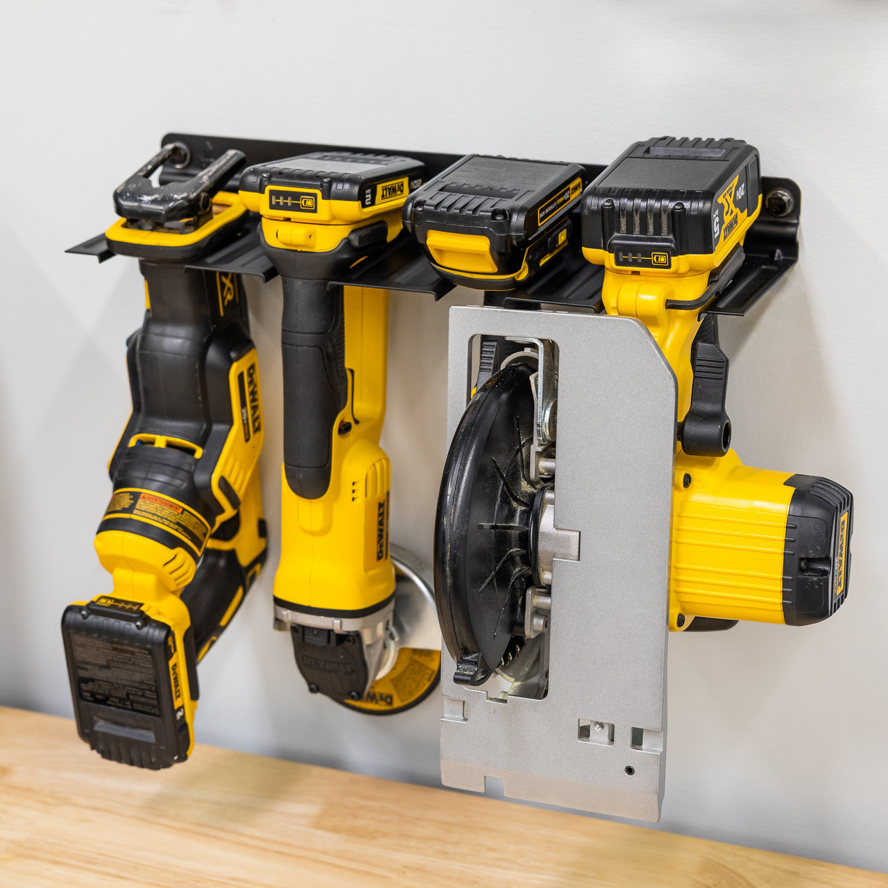E-Power Tool Organizer | Garage Storage Rack, wall-mounted and black, neatly holds three yellow and black DEWALT cordless tools and two batteries above a light wooden workbench for efficient, organized storage.