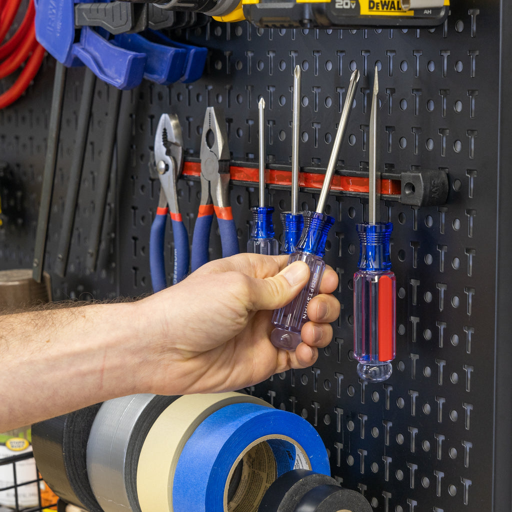 A hand grabs a screwdriver from the Pegboard Pro Accessory Pack, which organizes pliers, clamps, and tape rolls on a metal pegboard—keeping the workspace efficient, neat, and organized.