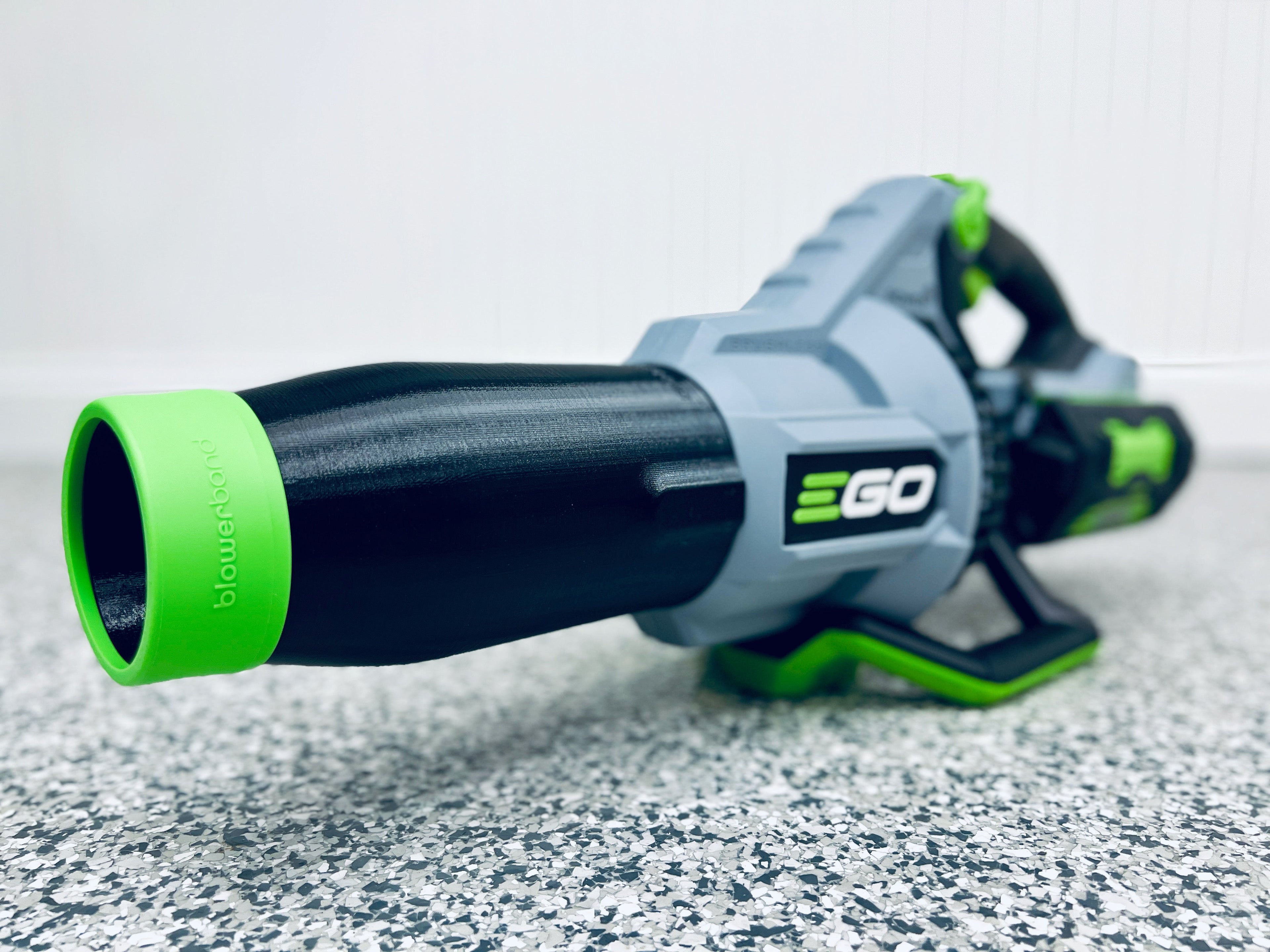 A close-up of an EGO leaf blower with a STUBBY® Car Drying Nozzle for 765, 670, 650, 615, 580, 575 & 530 CFM models rests on a speckled gray floor against a white wall.