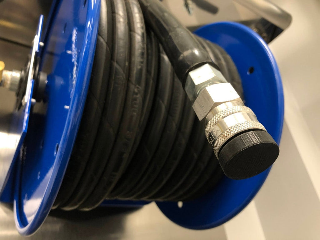 Close-up of DribbleStopper Plug for Pressure Washer & Garden Hose Quick Disconnect Fittings on a blue reel with a metal connector, designed to prevent water leaks. Background is partially blurred.
