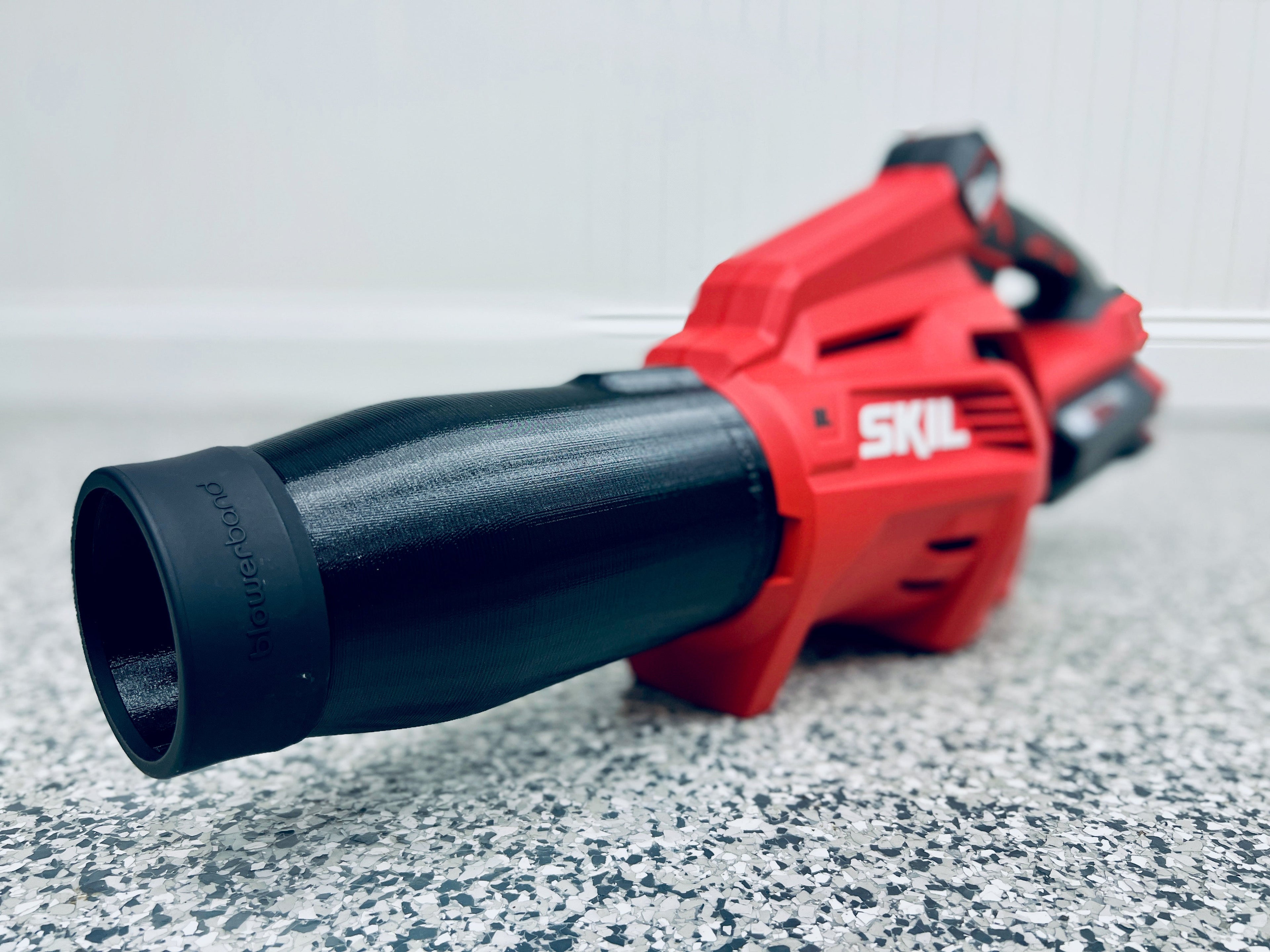 A close-up of a red SKIL PWR Core 40V leaf blower (BL4713C-11) with the STUBBY® Car Drying Nozzle attached, resting on a speckled gray and white floor. The background is blurred.
