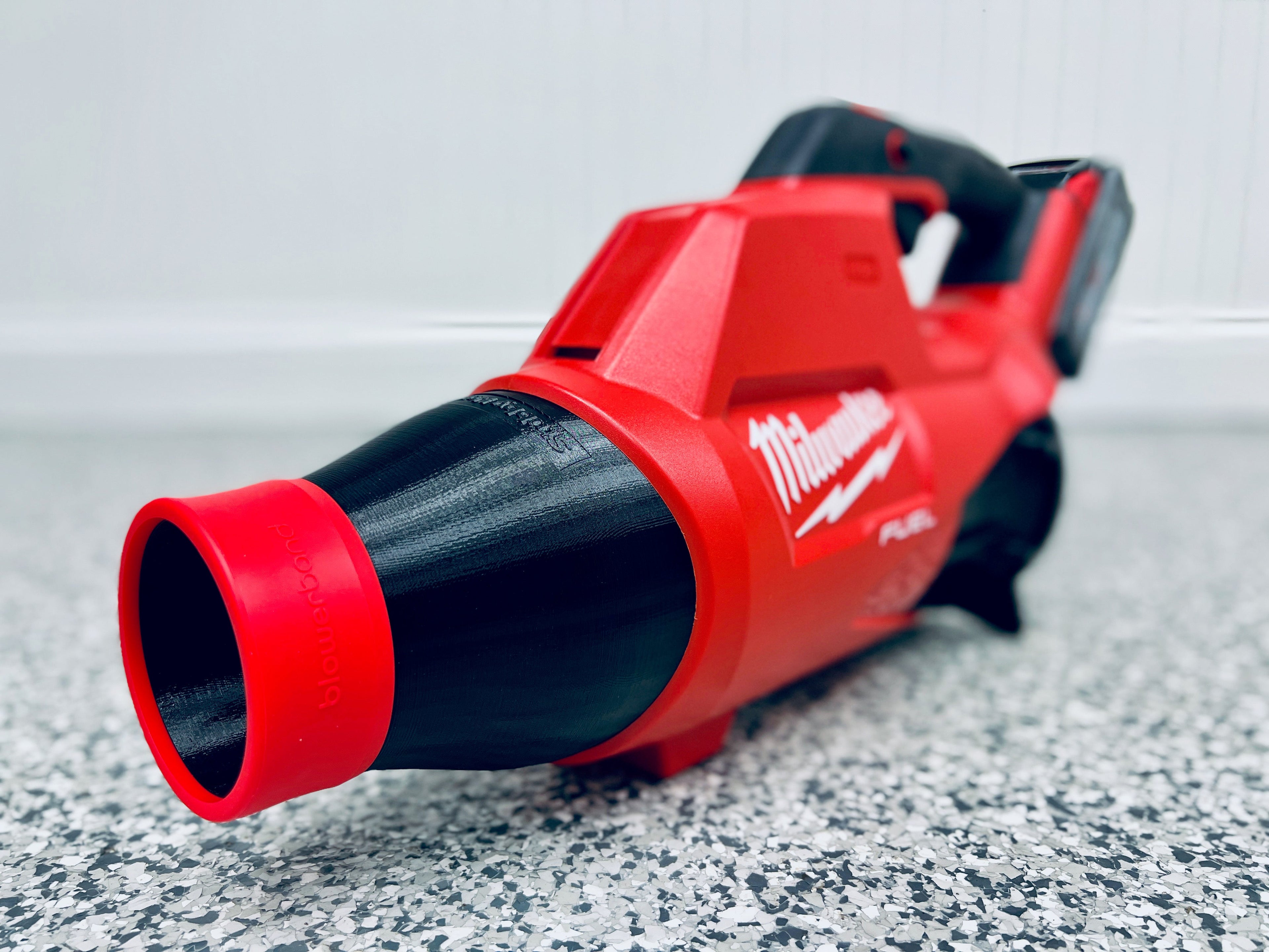 A close-up of a Milwaukee M18 FUEL leaf blower (2724-20) fitted with the STUBBY® Car Drying Nozzle, lying on a speckled gray floor with the nozzle in the foreground and handle in the background.