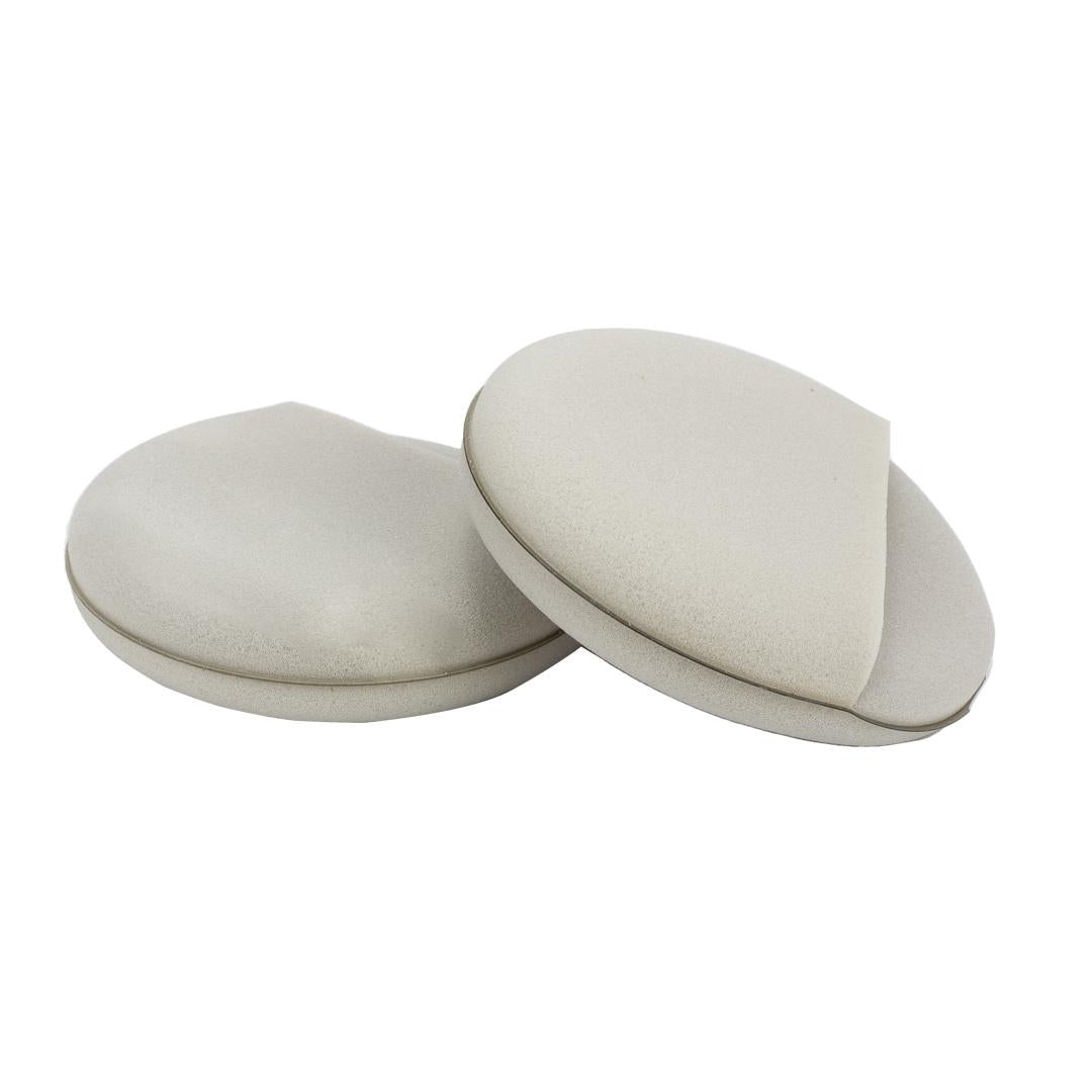 Two beige, oval-shaped Finger Hold Foam Wax Applicator pads with slight grooves are stacked partially overlapping on a white background. Comes as a 2 pack.