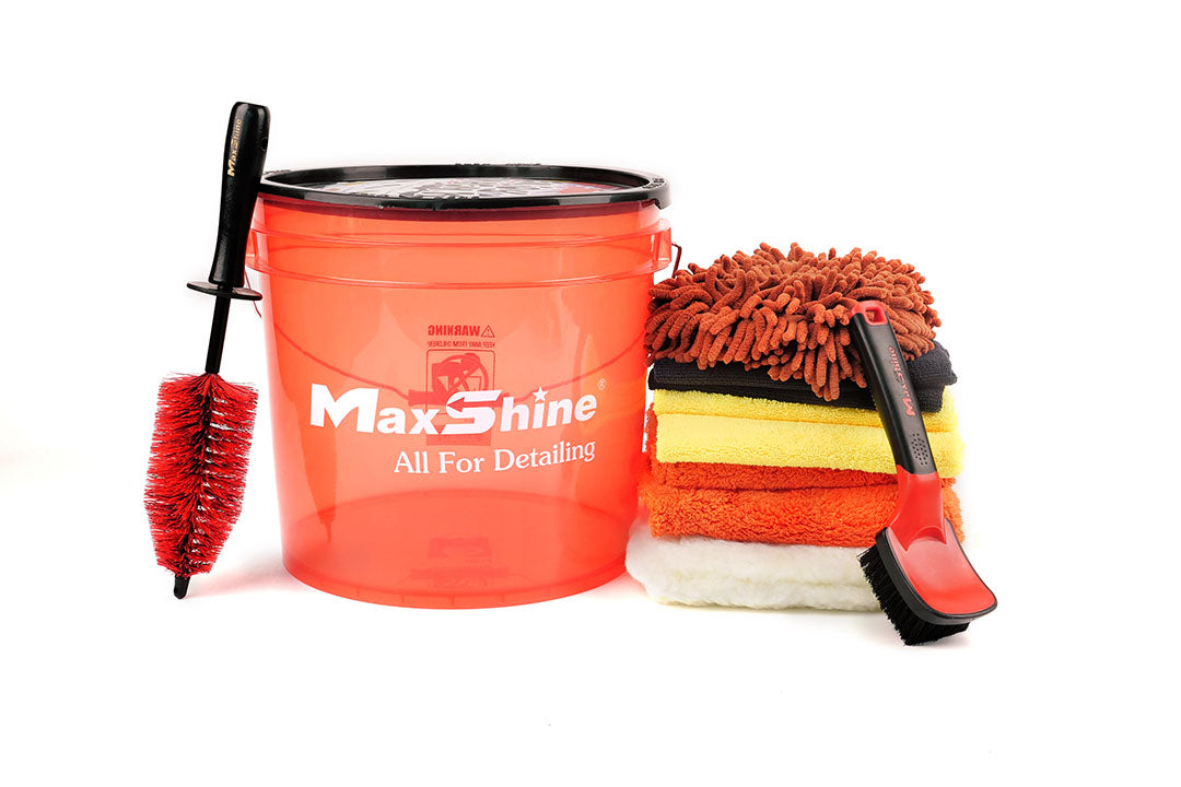 A red Enjoy Car Wash Bucket Kit sits beside a red and black wheel brush, colorful microfiber towels, an orange wash mitt, and a detailing brush—essential car cleaning tools on a white background.