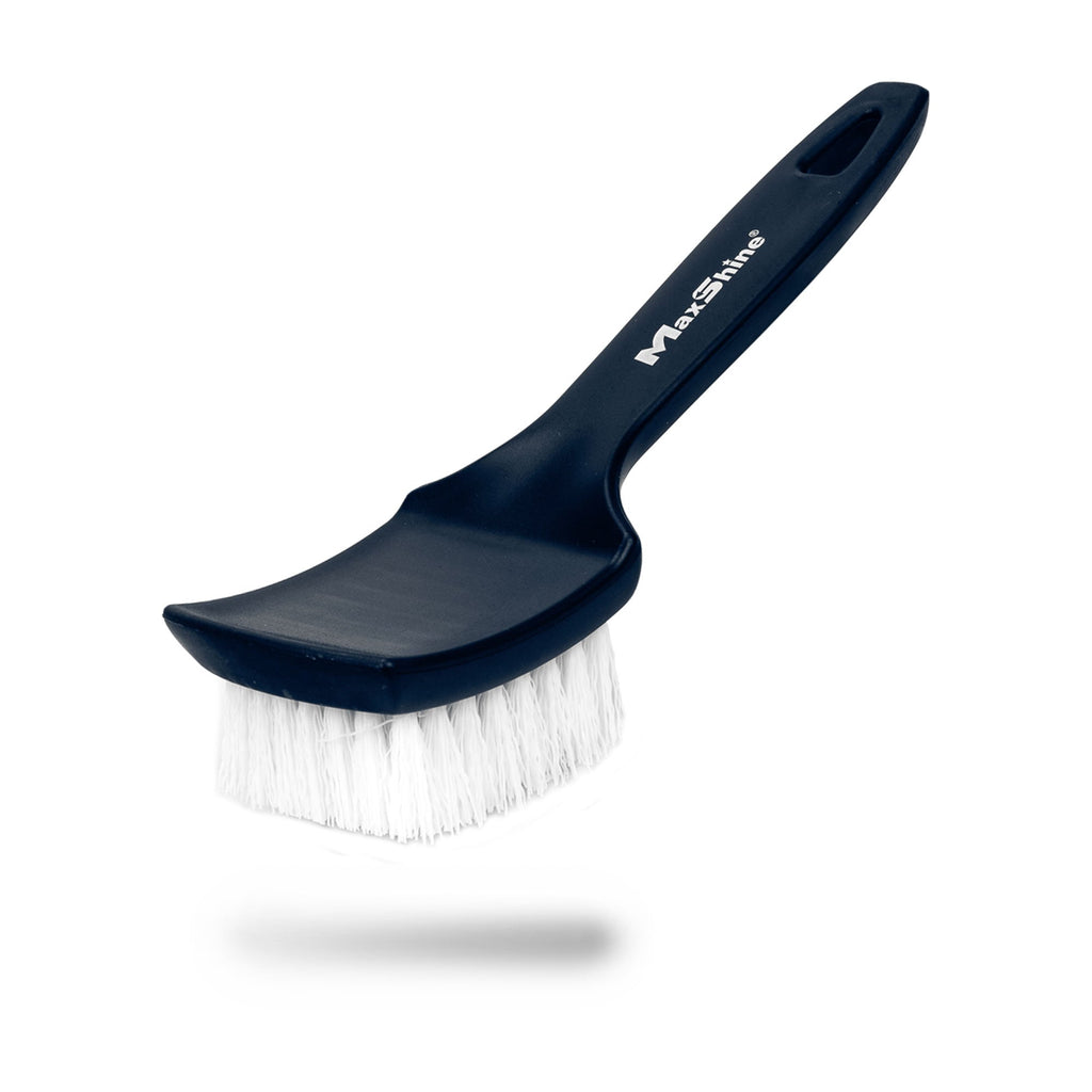 The Tire Scrub Brush, featuring stiff bristles and a curved handle with a hanging hole, is shown at an angle on a white background. The black brush casts a subtle shadow beneath it.
