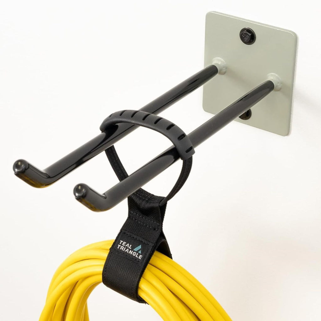 A Bedrock Garage Wall Hook (Cactus, heavy-duty) is mounted to a white wall with two screws, holding a coiled yellow extension cord secured by a black strap.