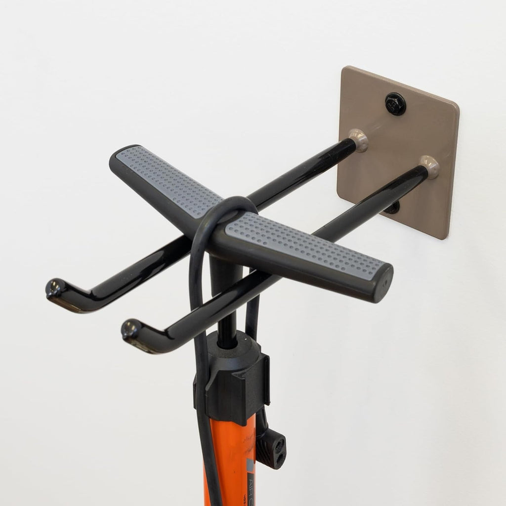 The Bedrock Garage Wall Hook | Heavy-Duty | Mud features two black metal arms that securely hold an orange bicycle pump on a white wall, providing a practical garage storage solution.