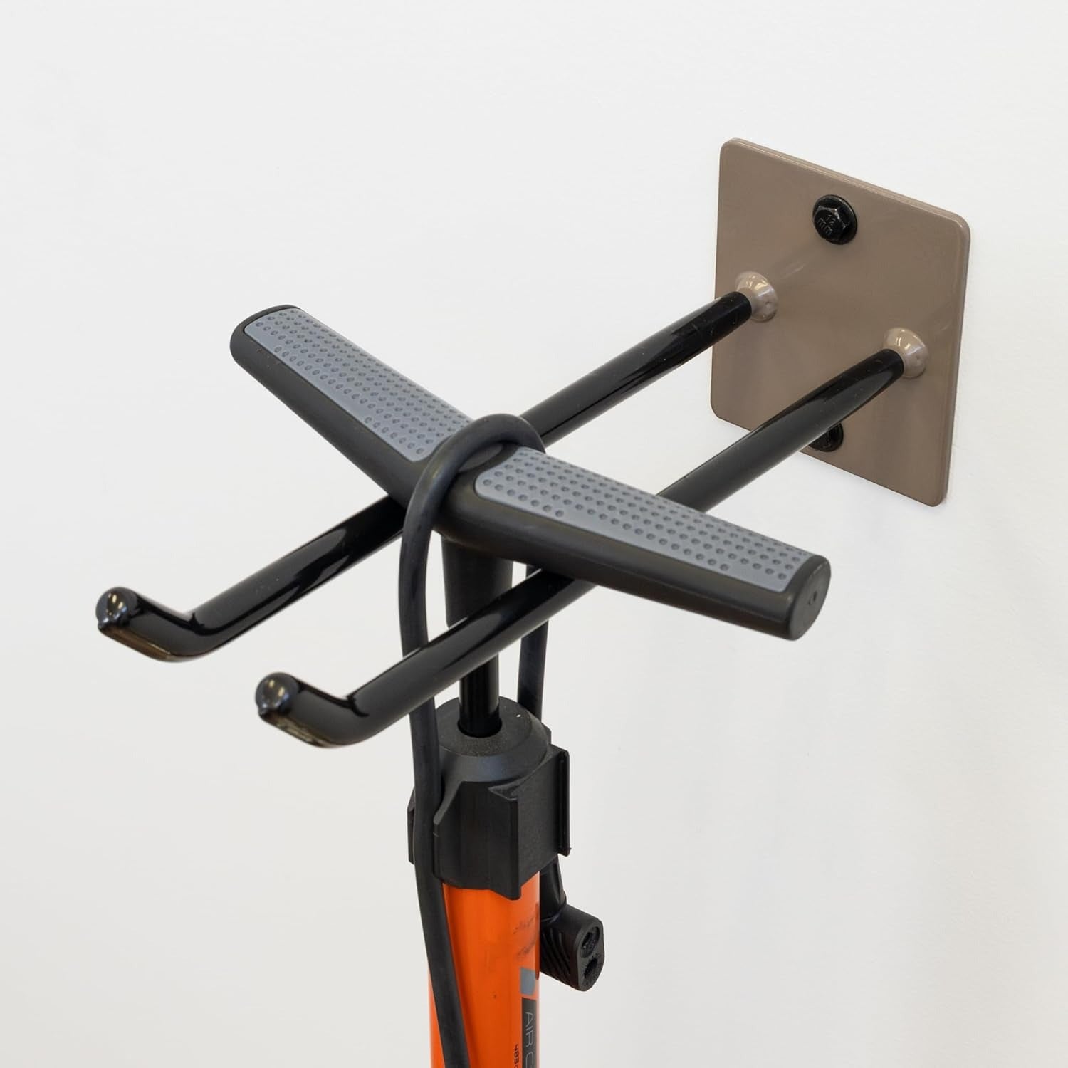 The Bedrock Garage Wall Hook | Heavy-Duty | Mud features two black metal arms that securely hold an orange bicycle pump on a white wall, providing a practical garage storage solution.