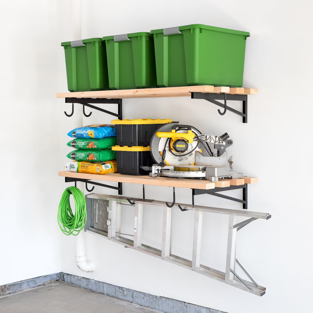Two 2' x 4' DIY Wall Shelf Brackets | Heavy Duty Garage Wall Shelves hold five green storage bins, garden supplies, a yellow and black toolbox, and a circular saw. A green hose and metal ladder hang below in this organized garage corner.