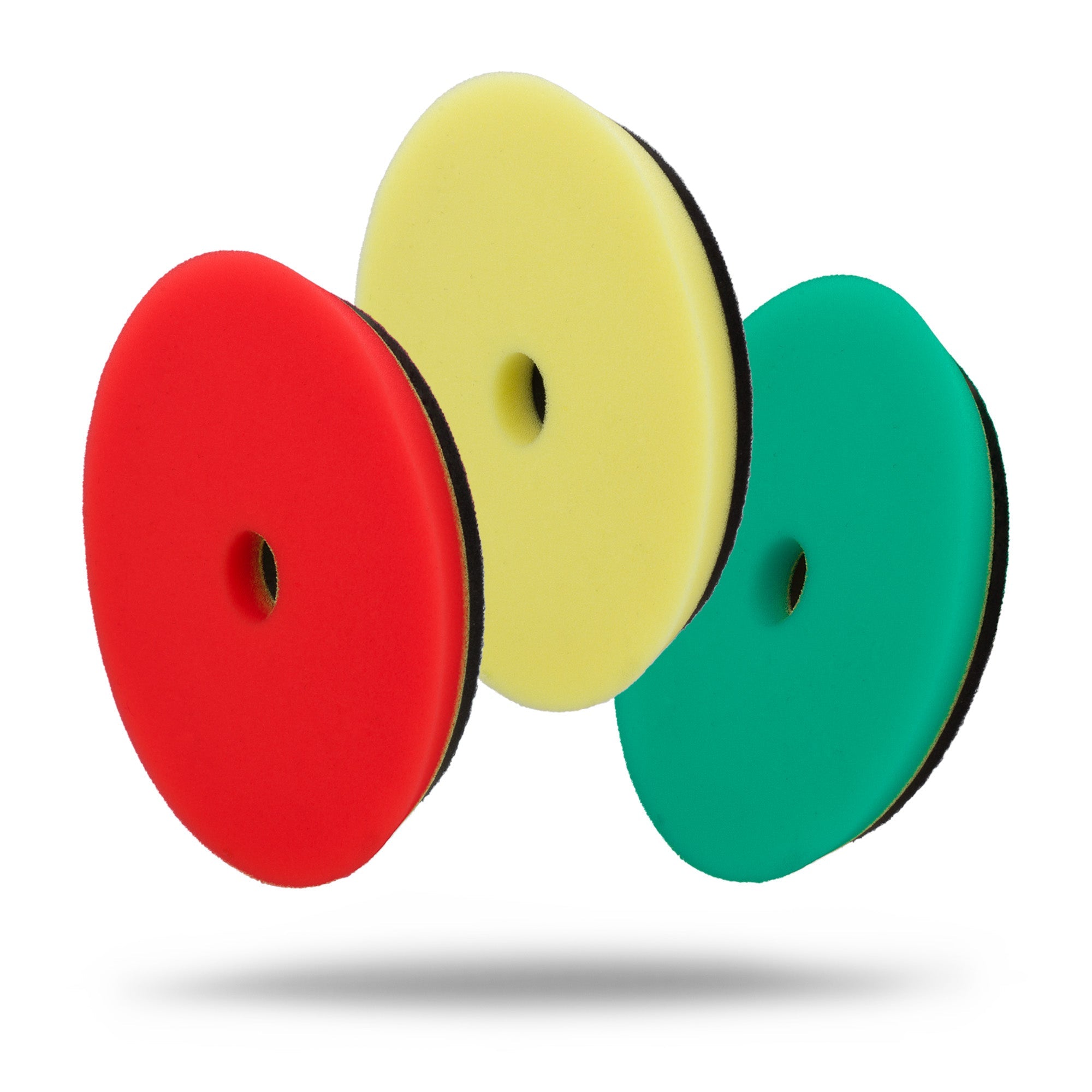 Three Low Profile Rubber Backed Foam Polishing Pads (5in, 6in) in red, yellow, and green with a central hole stand upright and lean against each other, casting shadows on a white background. Suitable for use with dual-action polishers.
