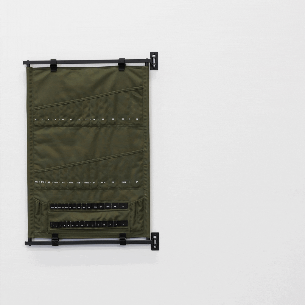 A Pivot Panel Tool Organizer in High Pine Green is mounted on a black frame against a white wall, featuring multiple labeled pockets that neatly store small black rectangular items for efficient, space-saving organization.