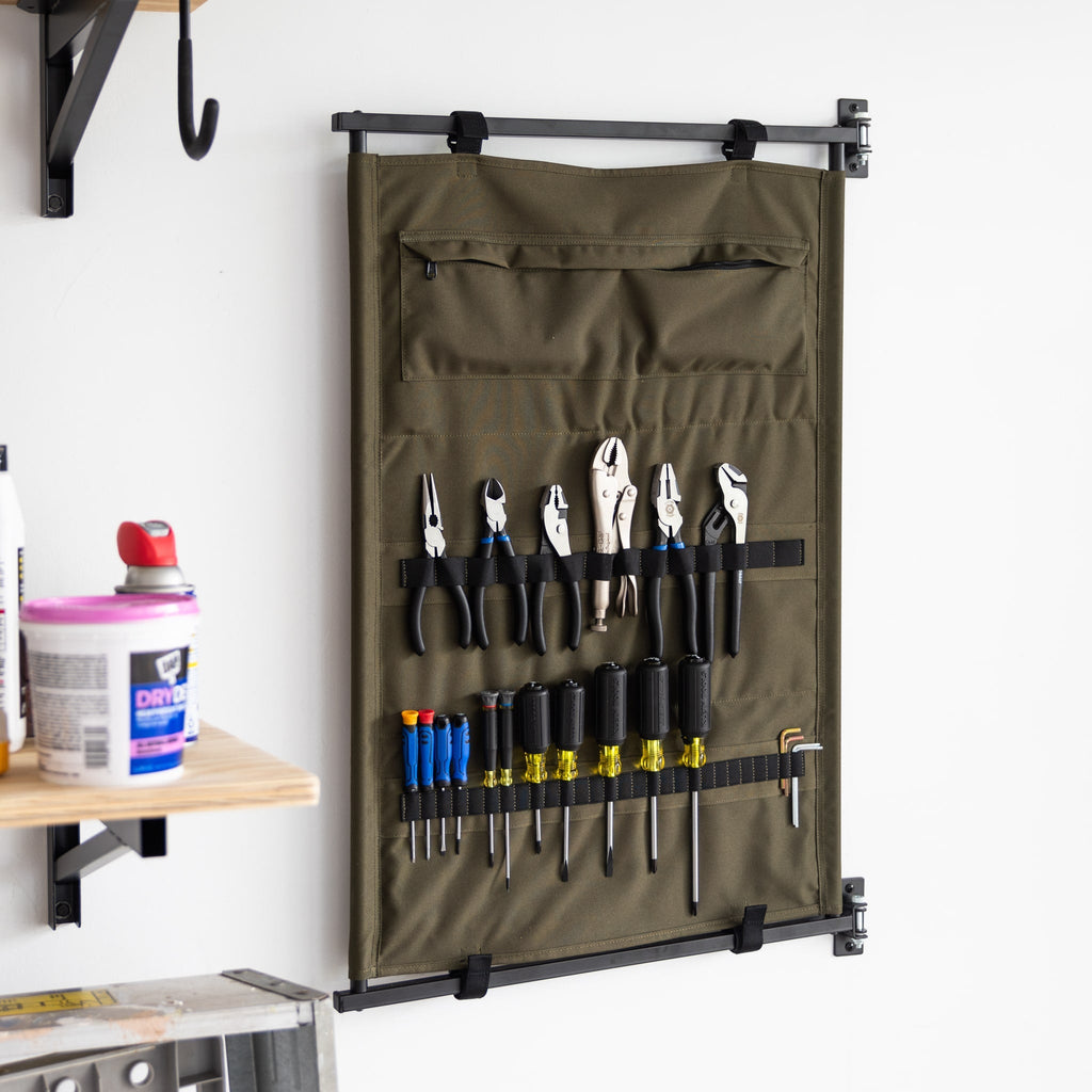 The Pivot Panel Tool Organizer in High Pine Green is wall-mounted, keeping pliers, screwdrivers, and wrenches accessible and organized. Partially visible shelves with containers sit to the left for extra storage.